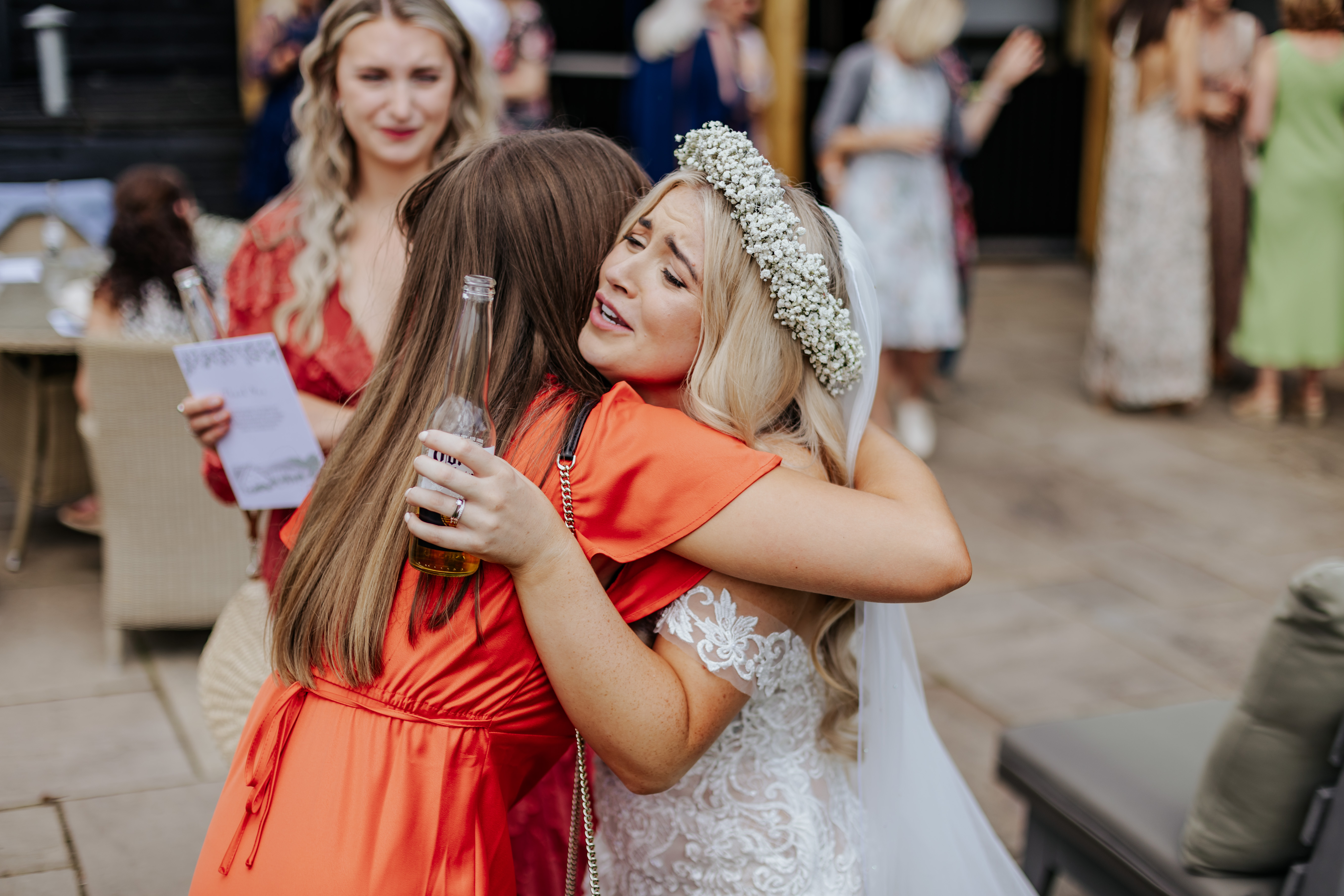 Bride hugs a guest with a beer in hand during their drinks reception