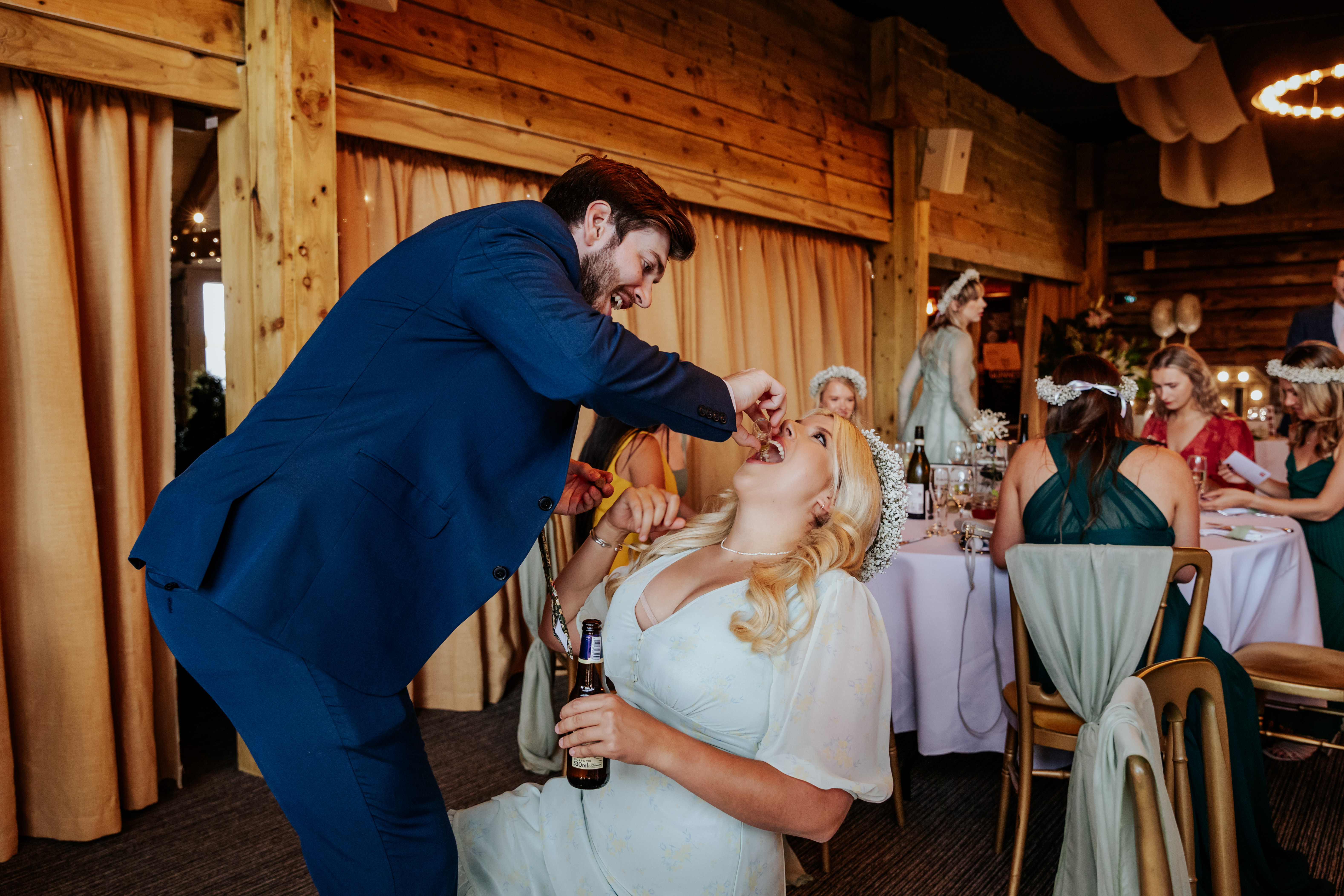 A groomsman pours a shot into a bridesmaid's mouth