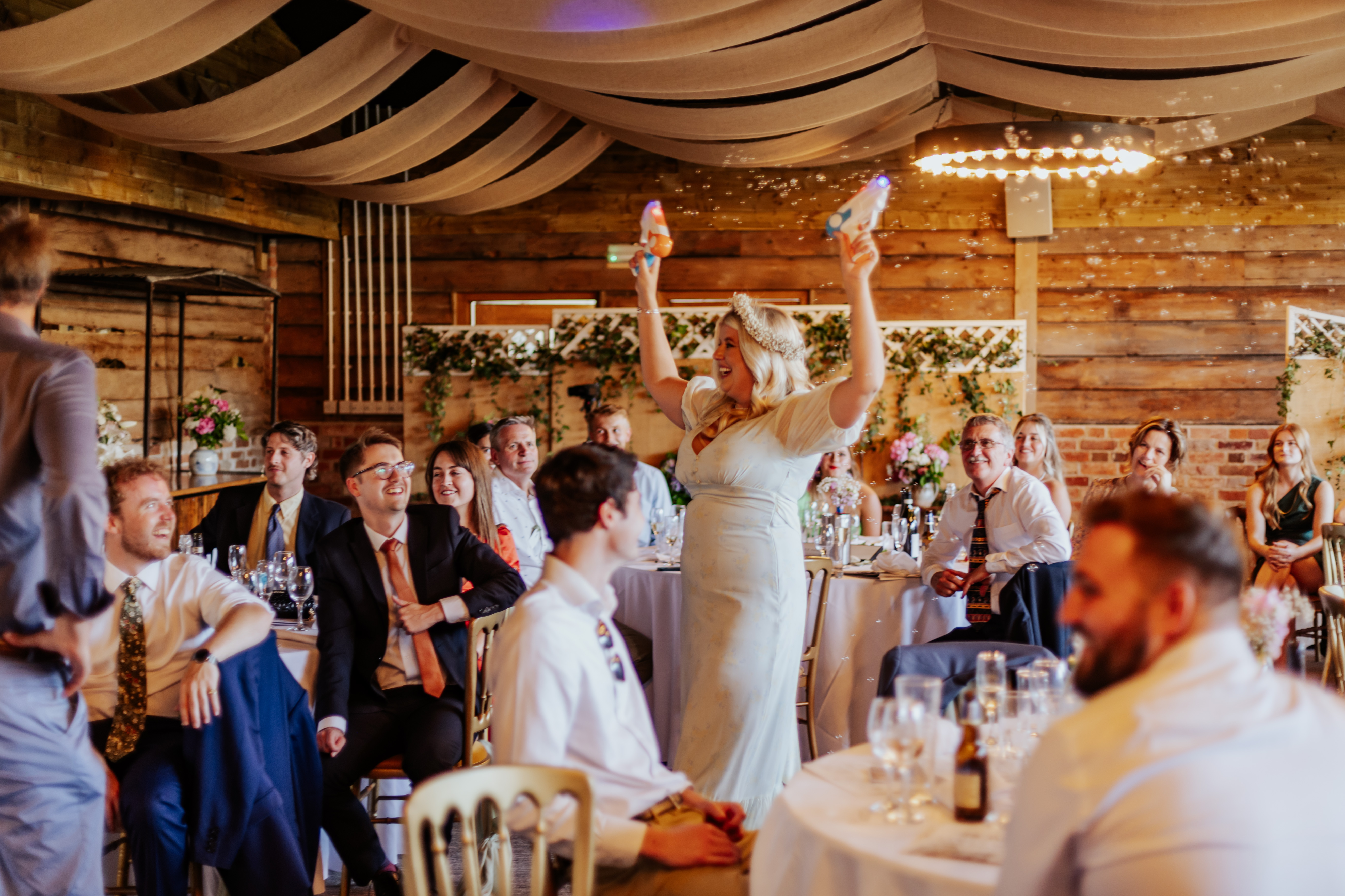 Bridesmaid runs between tables with bubble guns at Wellington Barn