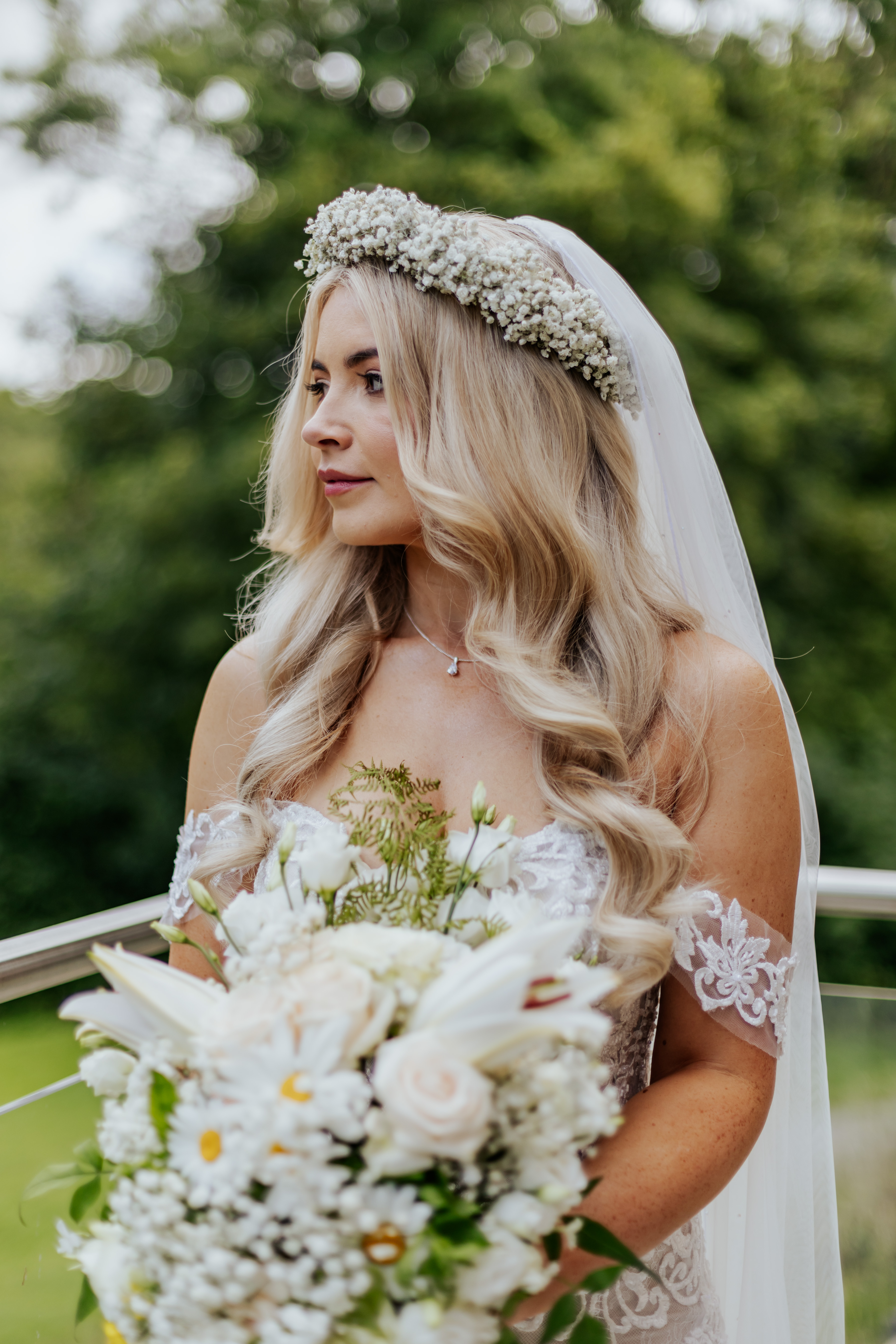 Bride Frankie looking out over a pond in her wedding dress, holding her white bouquet