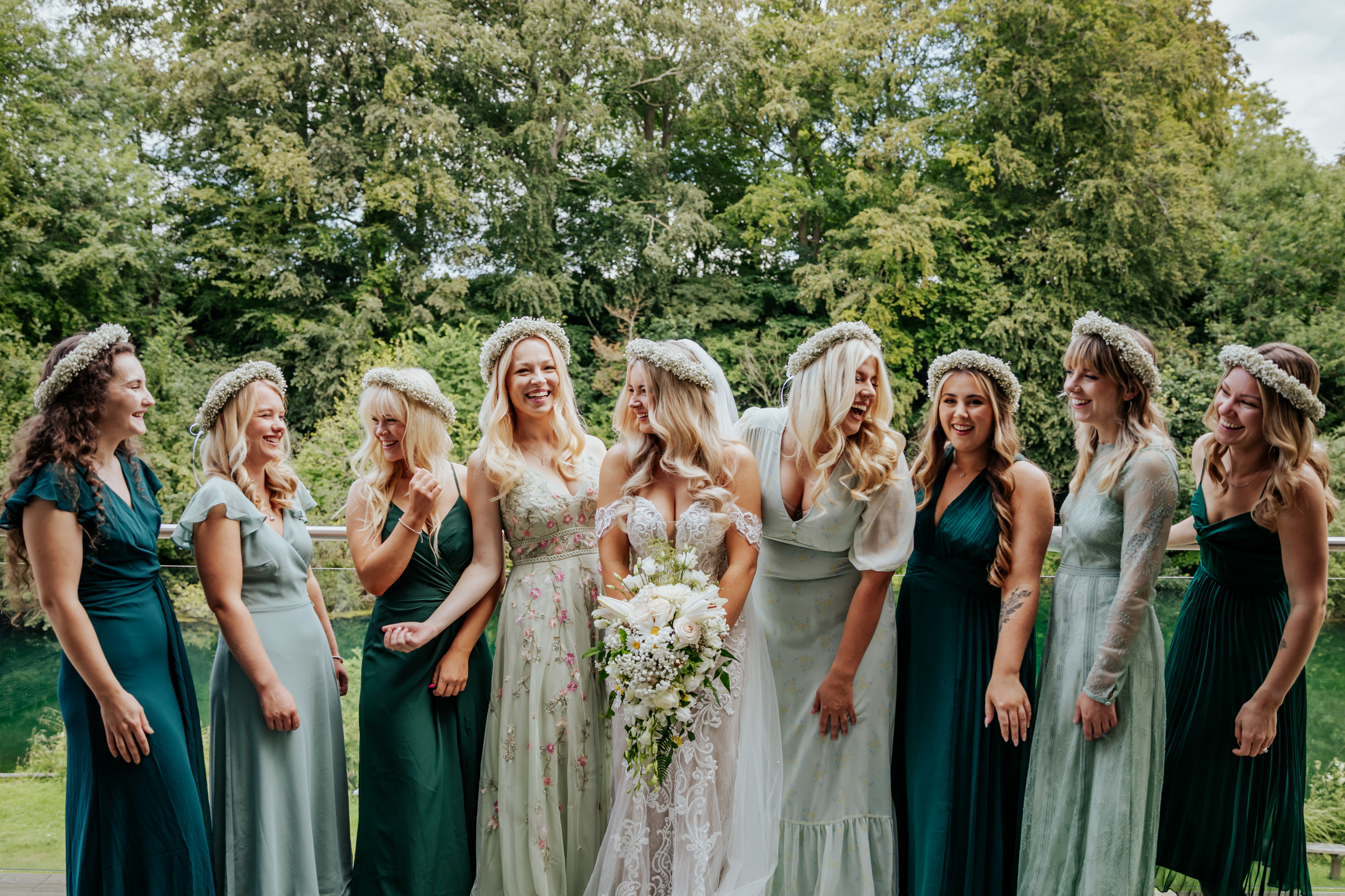 Bridal party laugh together, all wearing different shades of green with the bride in the centre