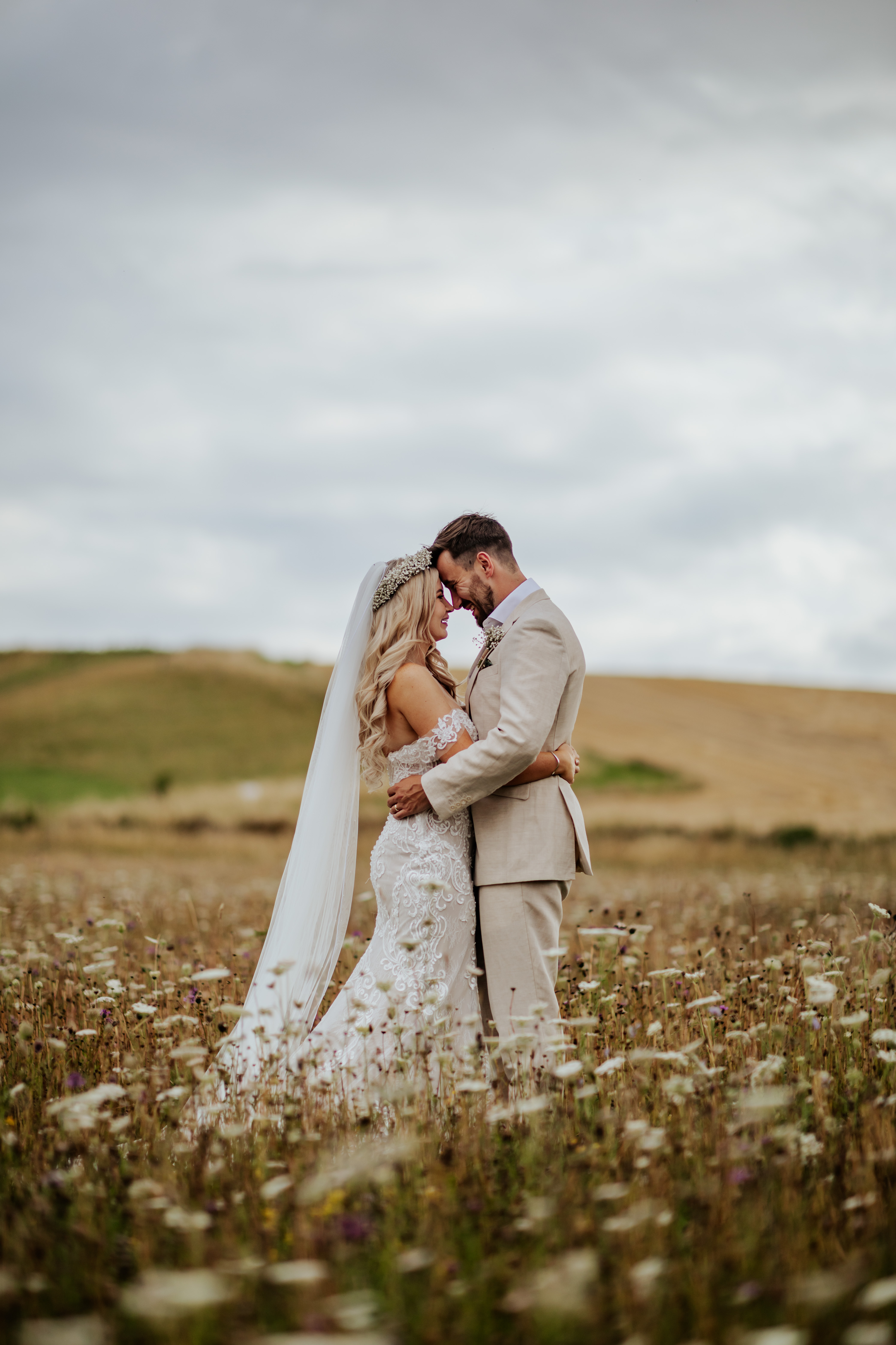 Bride and groom stand in a field of wildflowers with their foreheads together