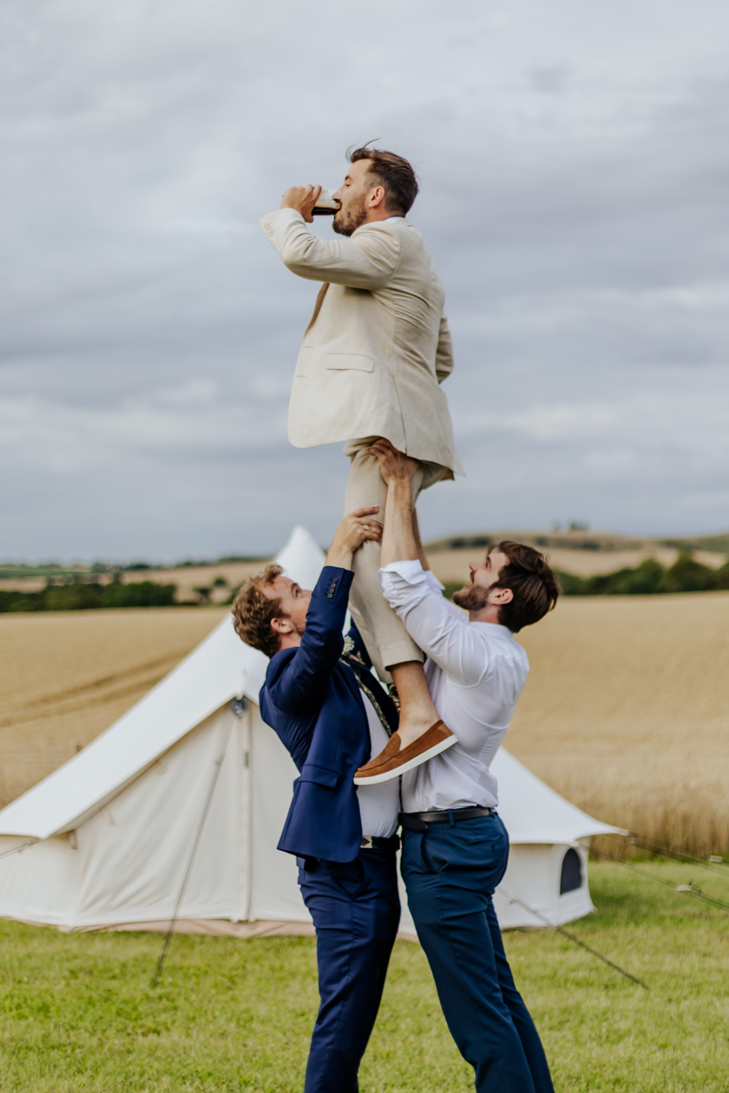 Two groomsmen rugby lift the groom while he drinks guinness