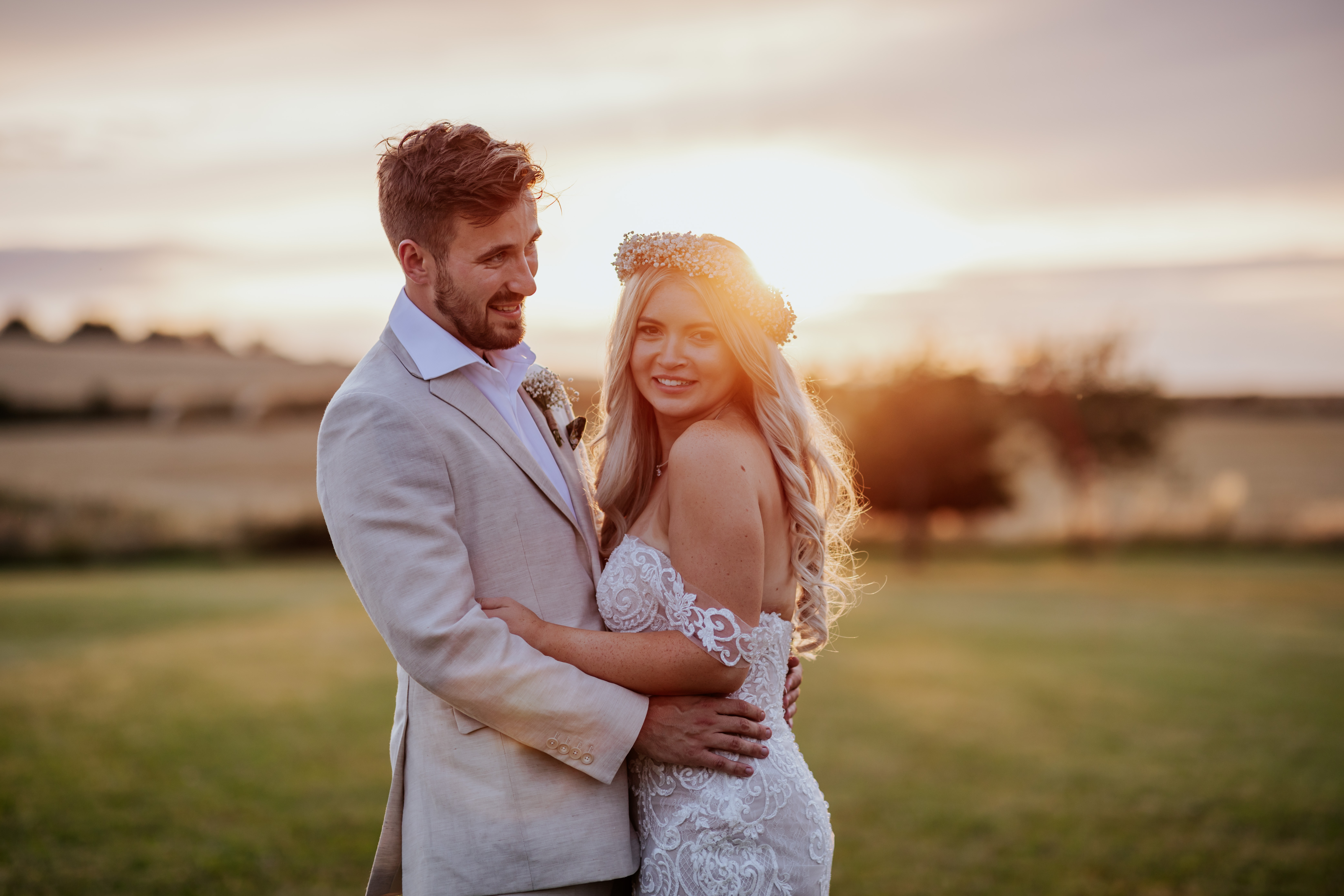 Bride and groom smile infront of a sunset at Wellington Barn