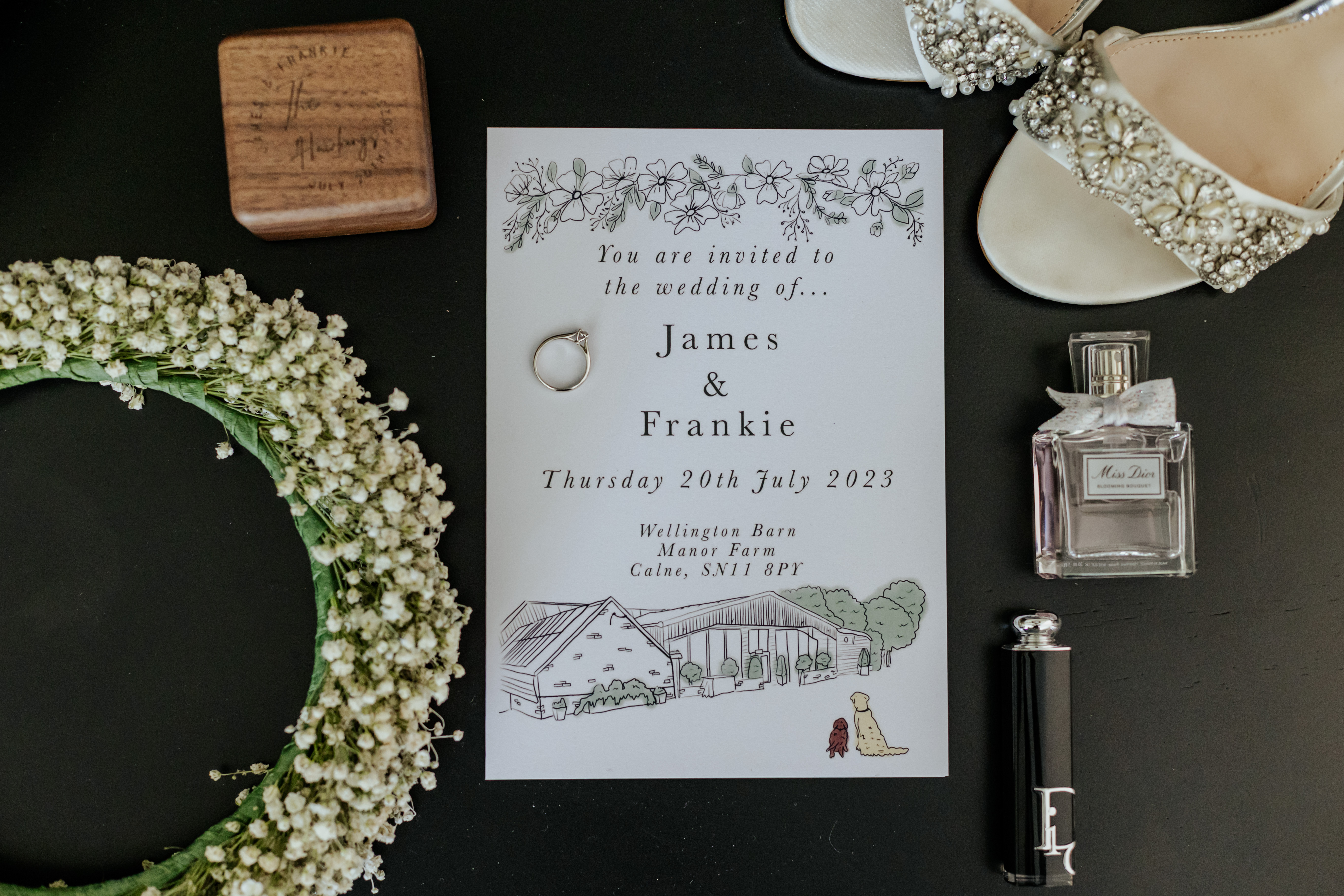 A flatlay of wedding stationery and bridal details, including shoes, perfume and a flower crown